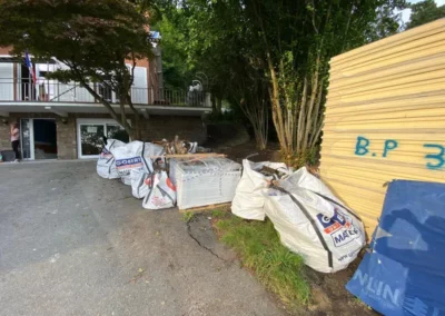 Évacuation des sacs de déchets et des matériaux de construction stockés à l'extérieur d'une maison. Les débris proviennent du démontage de l'ancienne couverture et l'installation de nouveaux matériaux isolants et de panneaux solaires.