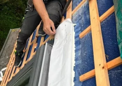 Un ouvrier de TS Rénovation réalisant les finitions d'étanchéité sur la partie supérieure d'une fenêtre de toit Velux installée sur la toiture à Mons. Ces finitions sont essentielles pour empêcher les infiltrations d'eau et maintenir l'intégrité de l'isolation de la toiture.