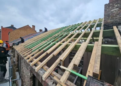 Rénovation de toiture à Roux.Les ouvriers sont en train de poser des chevrons sur les pannes en bois de la structure. Les chevrons sont alignés en diagonale pour préparer la future couverture de toit.