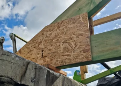 Renforcement des pieds de ferme d'une charpente. Un panneau de contreplaqué est utilisé pour rigidifier la structure, fixé sur une poutre en bois vert, assurant ainsi une stabilité optimale de la toiture. Ce renforcement fait partie des travaux réalisés par TS Rénovation pour restaurer la maison